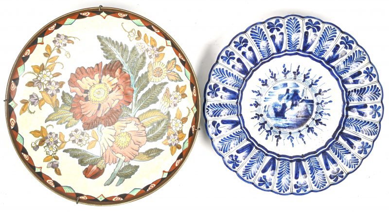 Een aardewerken Gouda plateelschaal met floraal decor, onderaan gemerkt. En een Delfts blauw-wit porseleinen sierschaal, onderaan gemerkt De Porceleyne Claeuw.