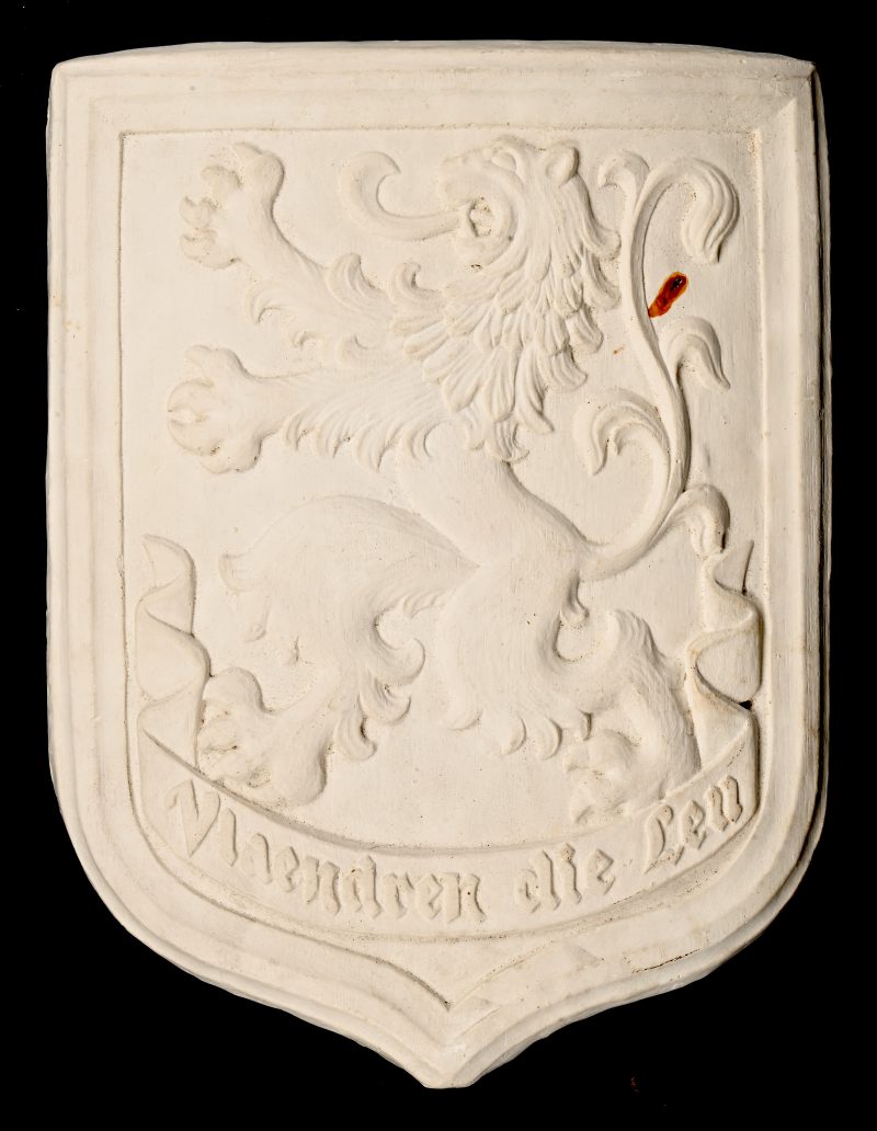 Een aardewerken wapenschild plaquette met opschrift; “Vlaanderen die Leu”.