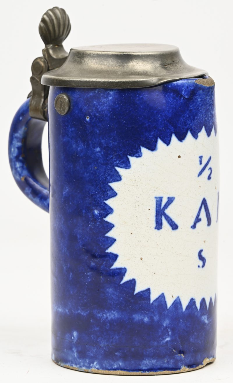 Een antieke keramische bierpul met een tinnen deksel, in blauw-witte kleurstelling met mogelijk jugendstil-elementen, afkomstig uit de late 19e tot vroege 20e eeuw.