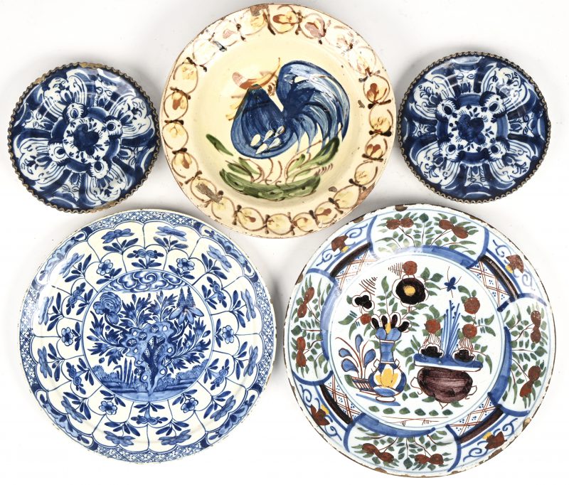 Een lot van vijf keramische borden, waaronder vier in Delftse stijl met blauwe decoraties en een Roemeense polychrome schotel met bloem- en vogelmotieven.