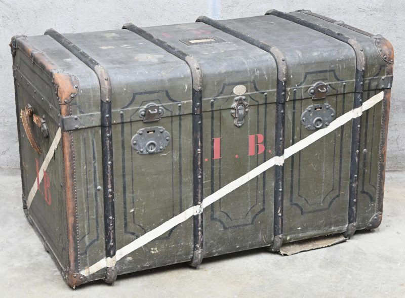 Een oude reiskoffer, gemerkt “Ange Faucq”. Met drie sloten en met binnenin uitneembare kledingladen.