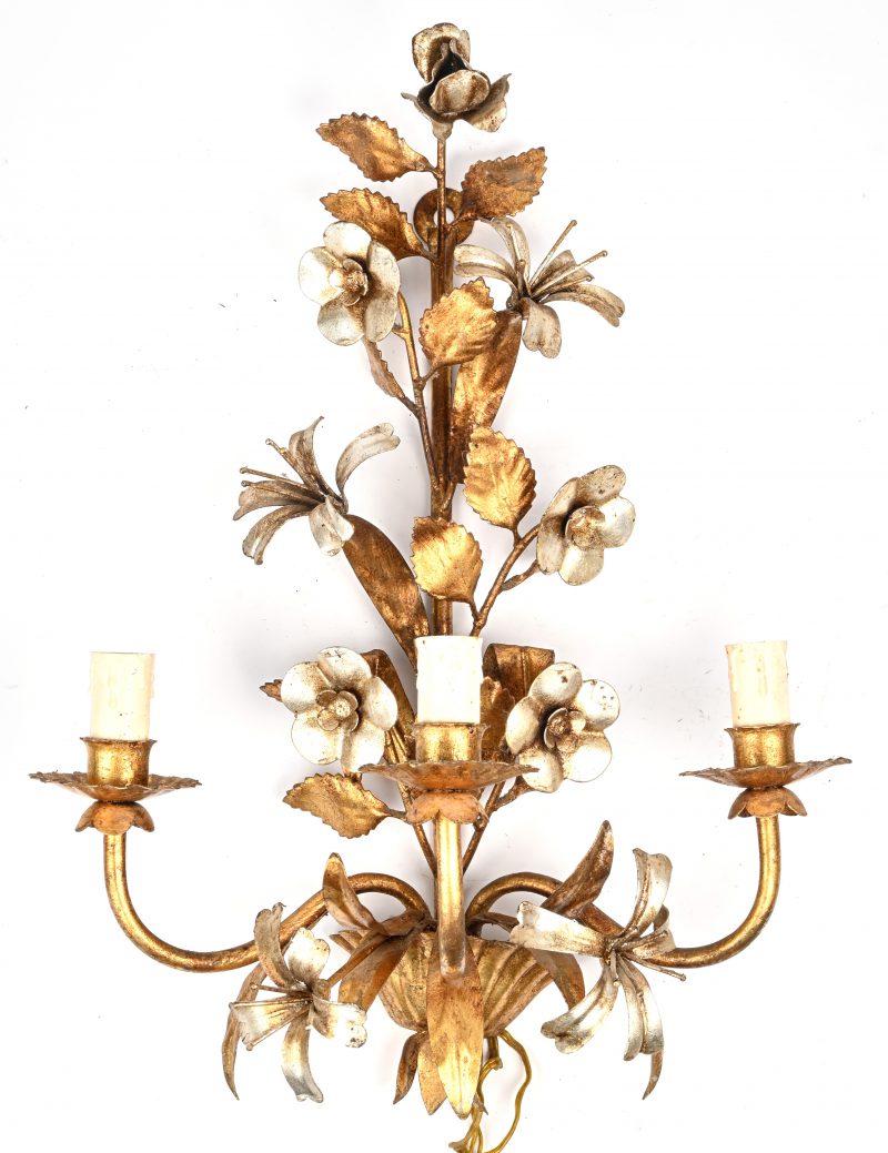 Een wandlamp met drie lichtarmen van verguld plaatijzer, versierd met bloemen en bladeren.