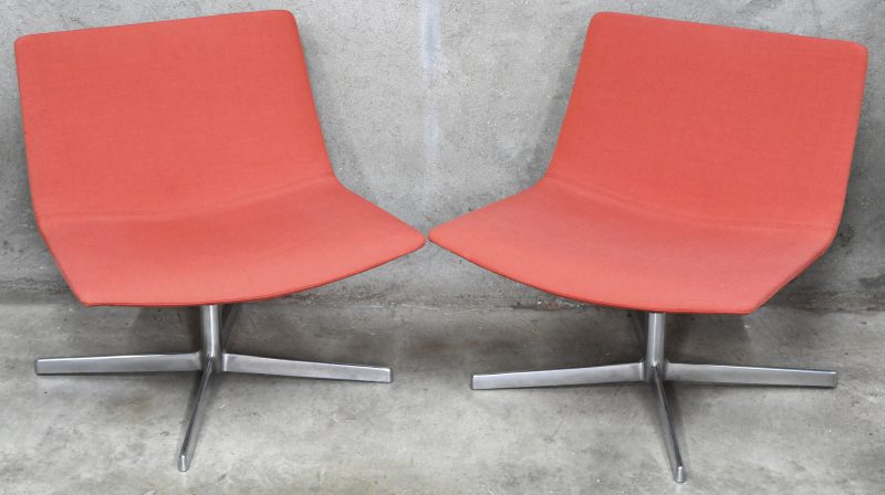 “Catifa 80”. Een paar design lounge draaistoelen met oranje gestoffeerde zitting en gechromeerde X-voet. Ontwerp door Lievore Altherr Molina voor Arper.