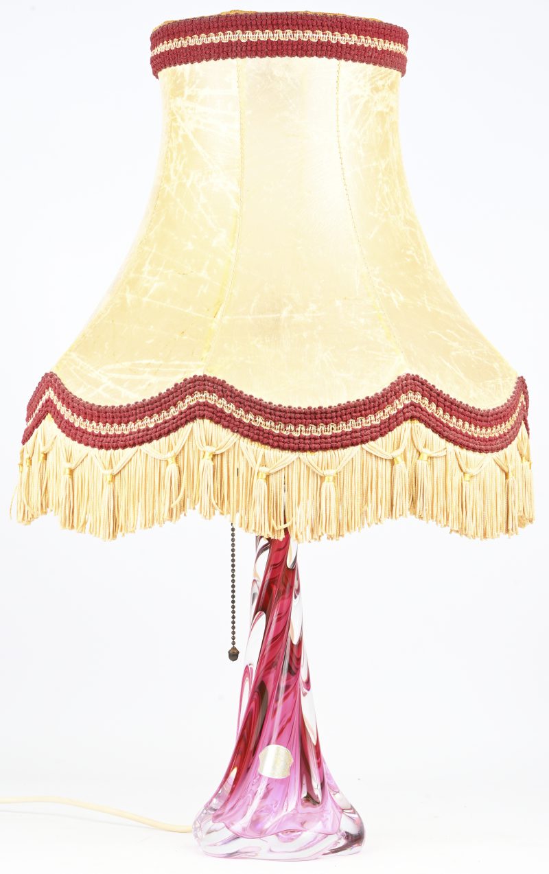 Een vintage kristalglazen tafellamp met rood in de massa. Onderaan gemerkt en draagt label. Kap in varkenshuid en gestoffeerde details. Scheurtje in de kap aanwezig.