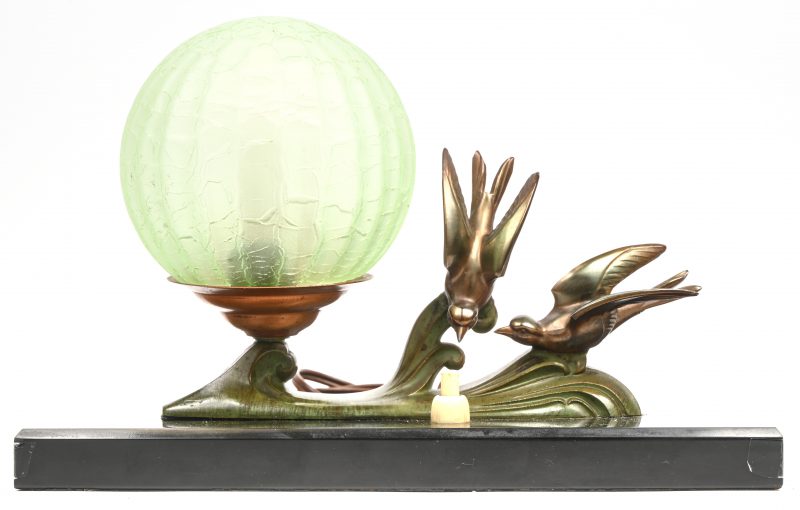 Een art-deco tafellampje met 2 bronzen zwaluwen en een groen glazen bolle blaker op een zwart marmeren voetje.