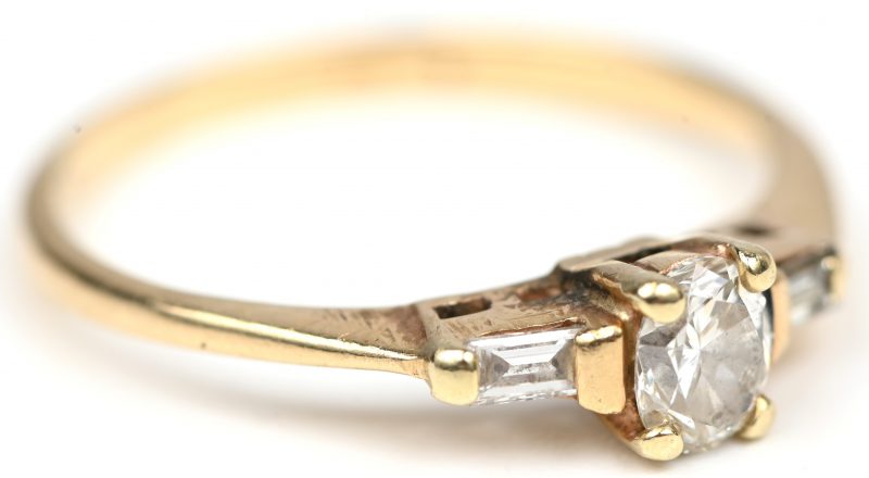 Een 14 kt geelgouden ring bezet met een centrale briljant en met twee diamant baguetten een gezamenlijk gewicht van +- 0,50 ct.