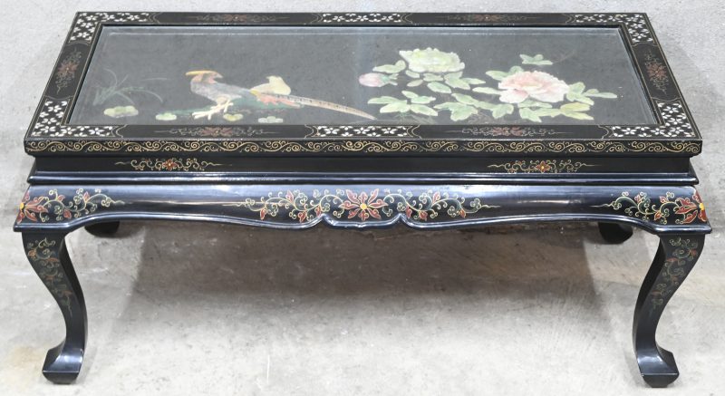 Een Chinees houten zwart gelakt salontafeltje met parelmoer inlegwerk en florale toetsen. Bovenop een glazen tafelblad waaronder een stilleven van pietradura op paneel met jade en speksteen.