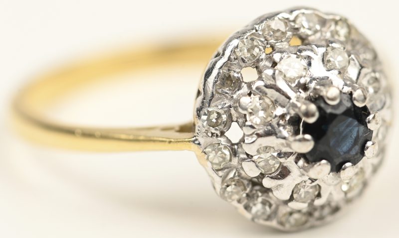 Een 18 kt wit en geelgouden ring bezet met diamanten met een gezamenlijk gewicht van +- 0,40 ct. en een centrale saffier van +- 0,20 ct.