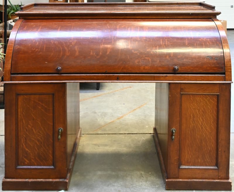 Een Engelse mahoniehouten rolltop bureau in Victoriaanse stijl met binnenin uitschuifbaar werkblad en lederen bekleding, 6 kleine laden en 7 vakjes. Onderaan aan weerskanten 1 deurkastje, verrijdbaar.