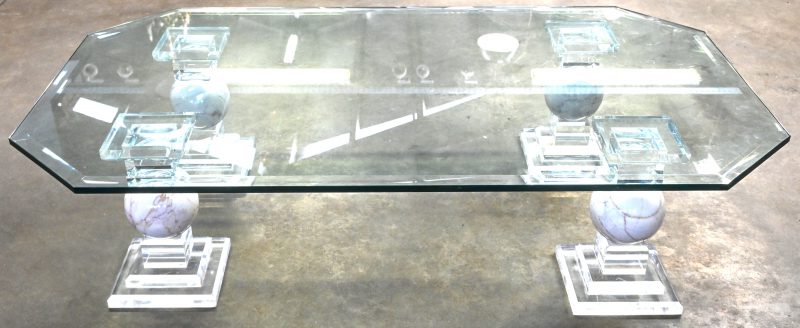 Een vintage salontafel met geslepen glazen blad en 4 poten in gehard plexiglas met marmeren bol in het center. Schilfertje aan het blad.