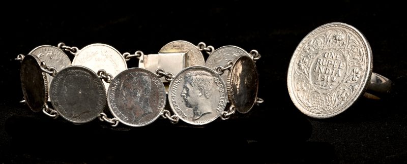 Een armband bestaande uit zilveren muntjes van 50 centimes met beeldenaar van Albert I evenals een ring bezet met een munt van 1 roepie d.d. 1919.