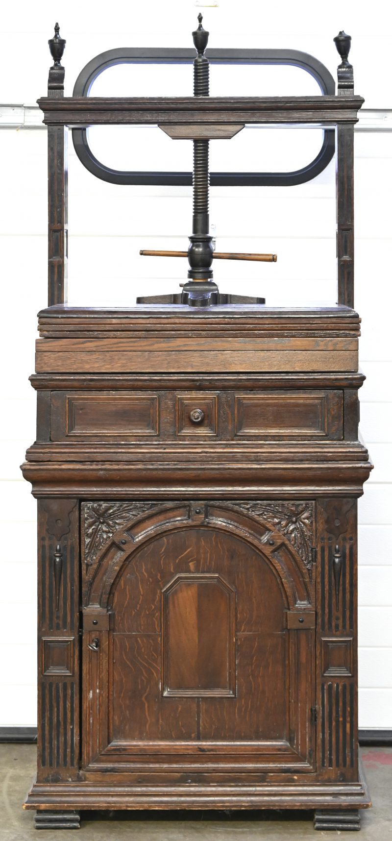 Een donker eikenhouten commode met 1 lade en 1 deurtje onderaan, en een linnenpers bovenop. Mechanisme van gedraaid hout, messing en smeedijzer. XIXde eeuw.