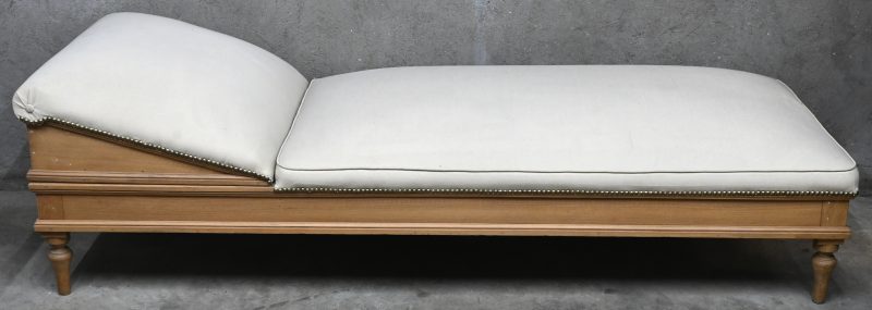 Een antieke chaise longue in hout en ecru stof bekleed.