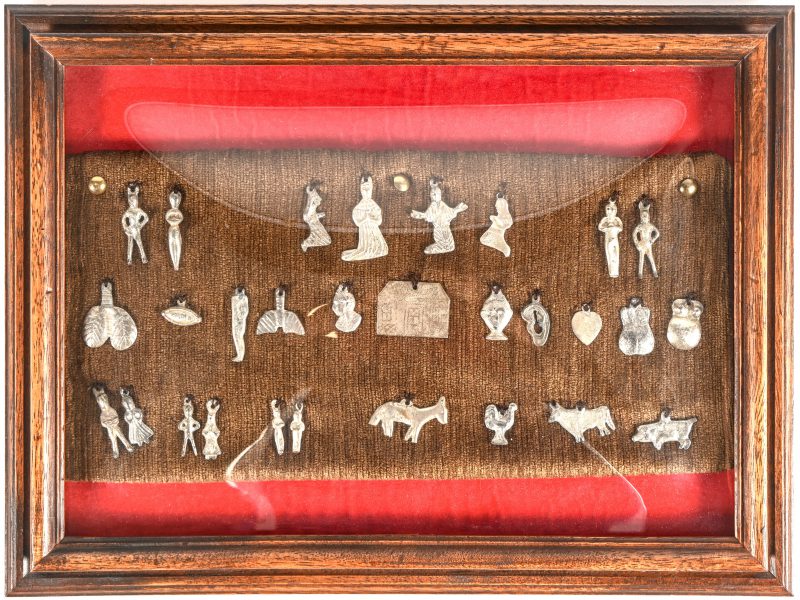 Een set van 29 Zilveren ‘Ex Voto’ uit Peru. in kader met gebombeerd glas.