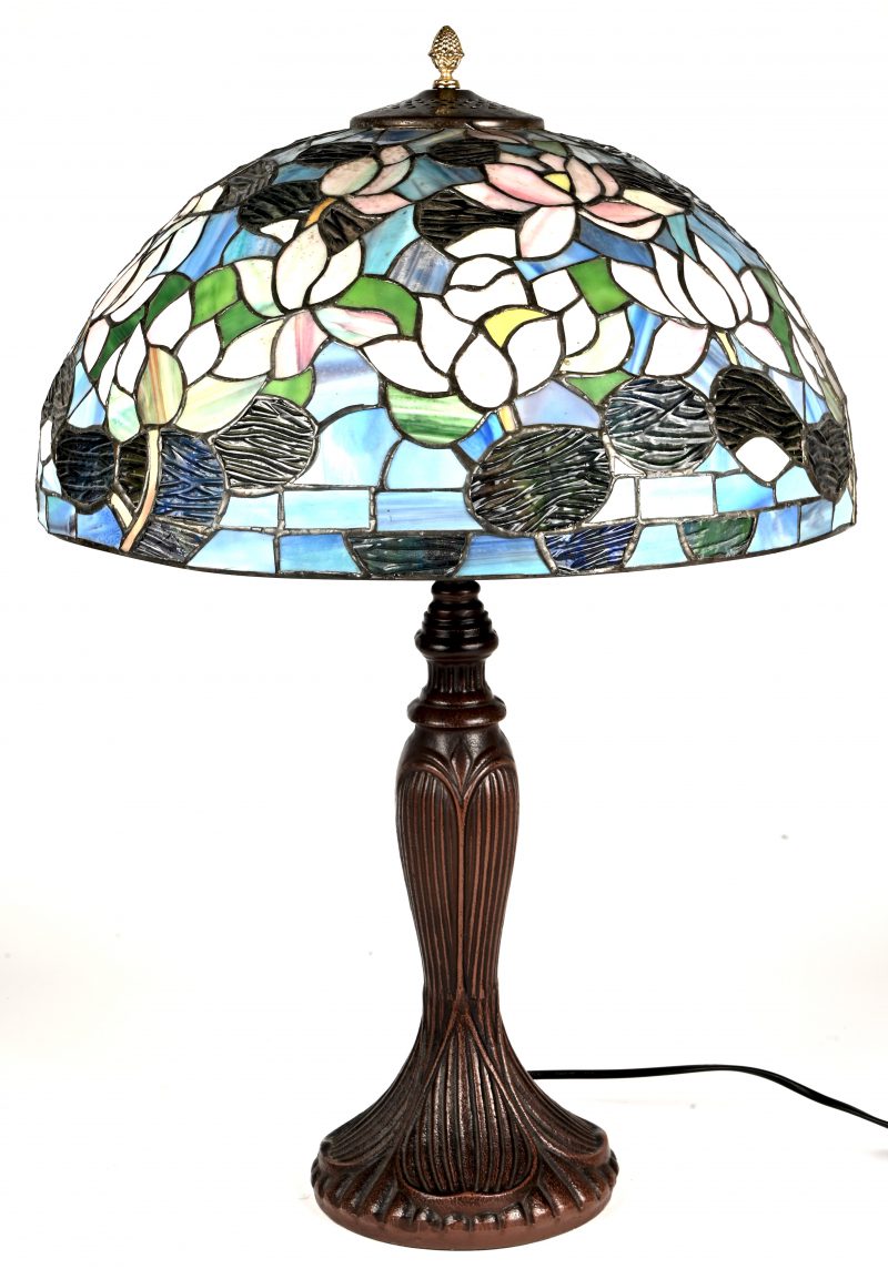 Een lamp in Tiffany stijl met gietijzeren voet en glas-in-lood kap met een decor van bloemen.