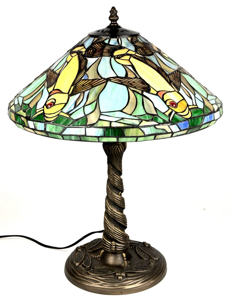 Een lamp in Tiffany stijl met bronskleurige voet en glas-in-lood kap met een decor van vliegende vissen en libellen op de voet.