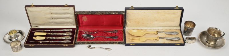 Een lot zilver bestaande uit een tas met ondertas met opschrift ‘Arnold’, een beker, een eierdopje met lepel en het opschrift ‘Guy’, 2 servetringen, een doosje met lepel en vork en 2 doosjes met serveerbestek waarvan enkel de heften in zilver.