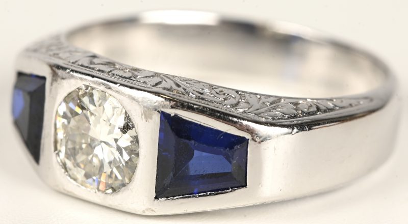 Een platina ring bezet met een centrale briljant van +- 0,90 ct. en twee saffieren met een gezamenlijk gewicht van +- 0,80 ct.