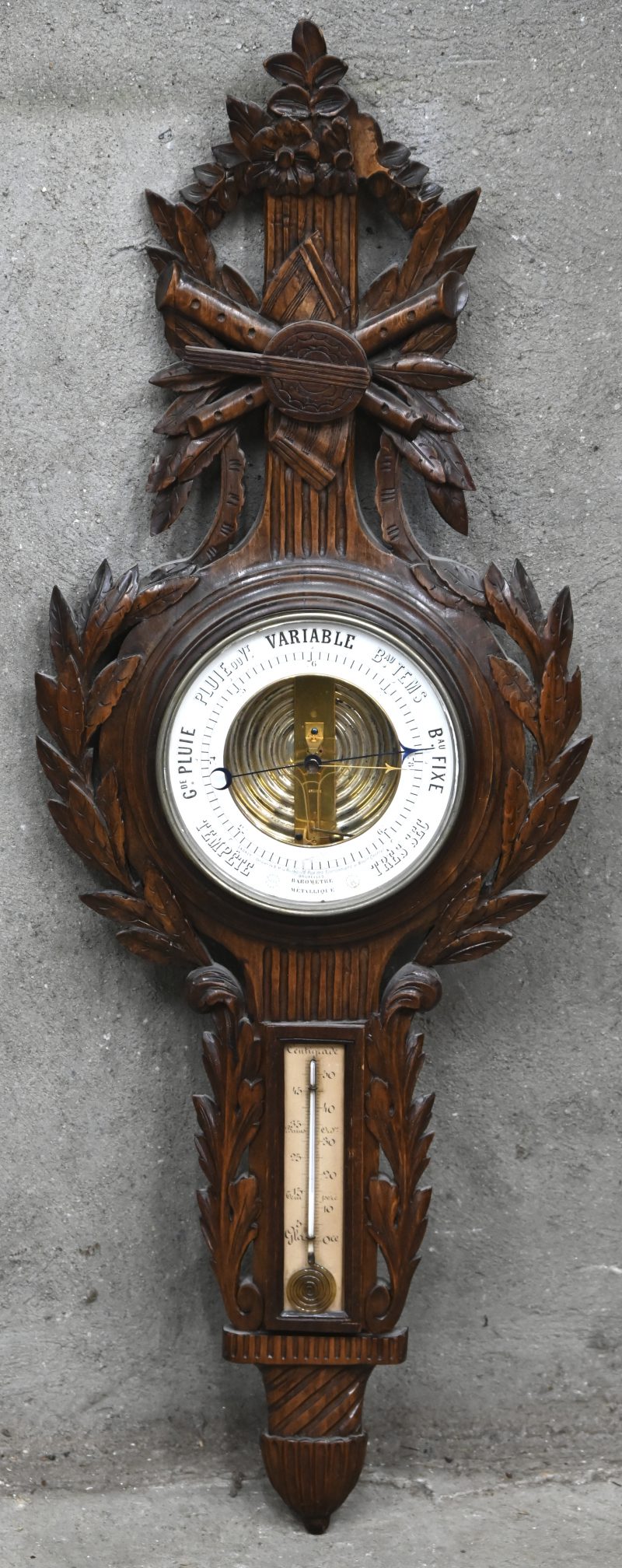 Een antieke barometer met houten kast. Decoratie in de vorm van muziekinstrumenten, lichte schade. Gemerkt in de wijzerplaat.