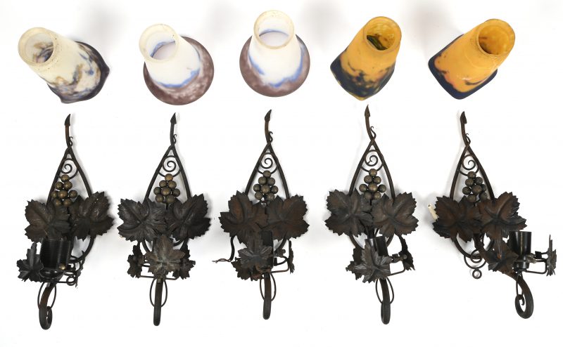 Een lot van 5 smeedijzeren wandarmaturen met druivelaar ornament, 1 lichtpunt en meerkleurig glazen blakers, waarvan 2 met barst of herstelling.