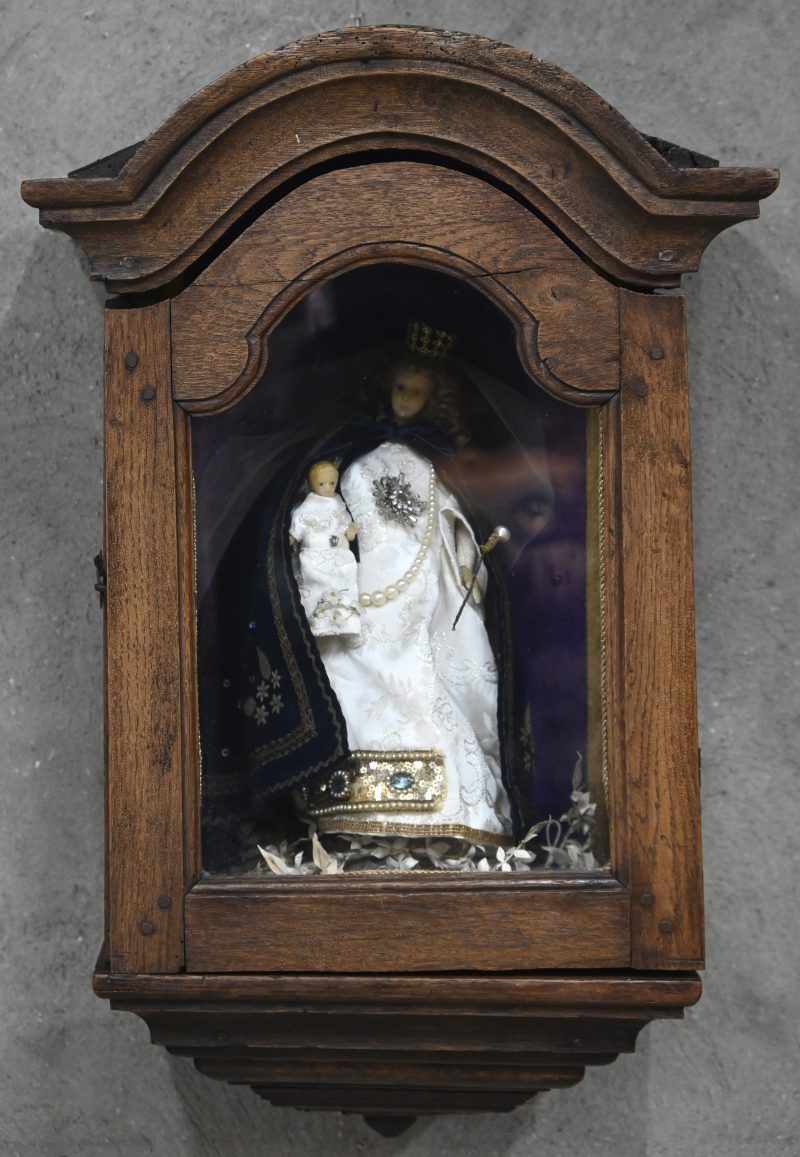 Een massief eikenhouten wandvitrine met hierin een wassen Madonna en kind.