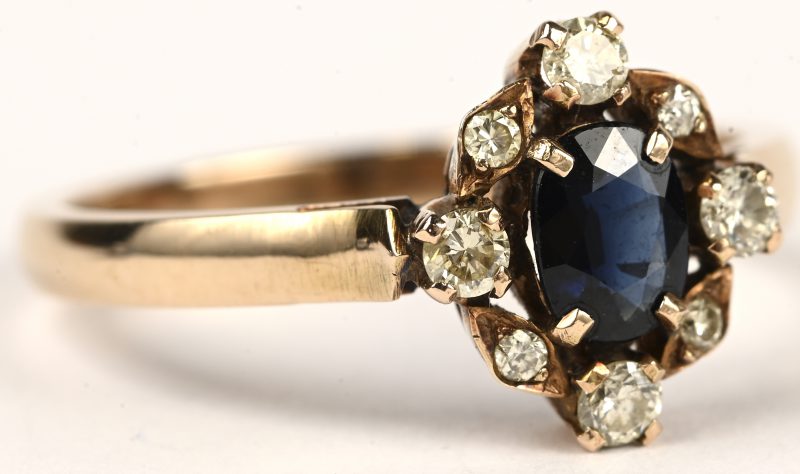 Een 14 kt geelgouden ring bezet met een centrale saffier van +- 0,40 ct. en briljanten met een gezamenlijk gewicht van +- 0,25 ct.
