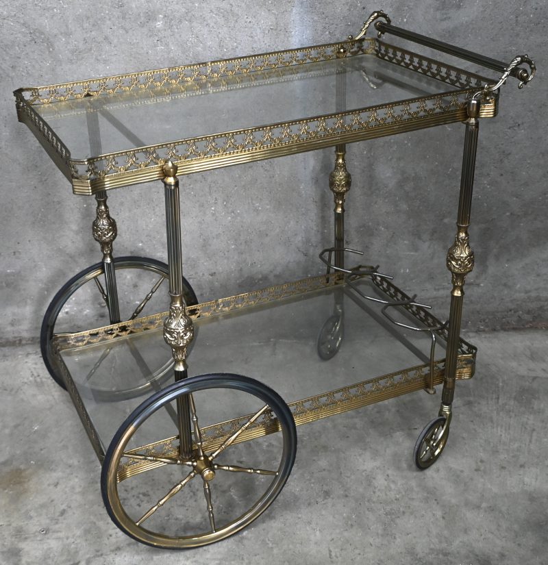 Een oude messingen bartrolley met glazen bladen.