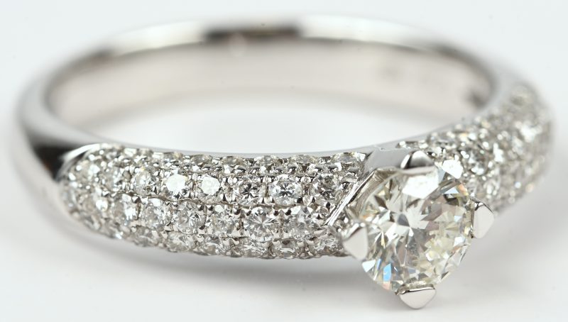 Een 18 kt witgouden ring bezet met een centrale briljant van +- 0,41 ct. en met briljanten met een gezamenlijk gewicht van +- 0,54 ct.