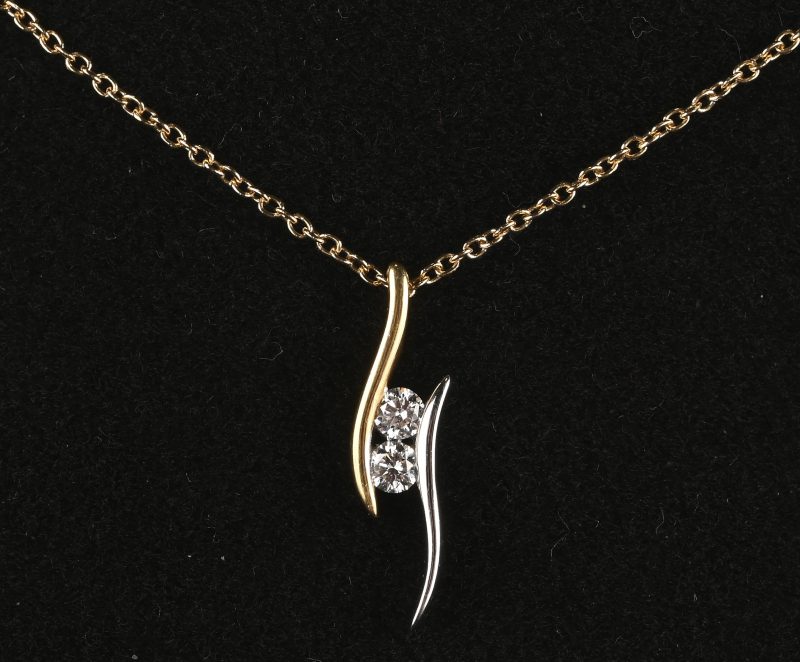 Een 18 kt wit en-geelgouden ketting met hanger bezet met briljanten met een gezamenlijk gewicht van +- 0,17 ct.