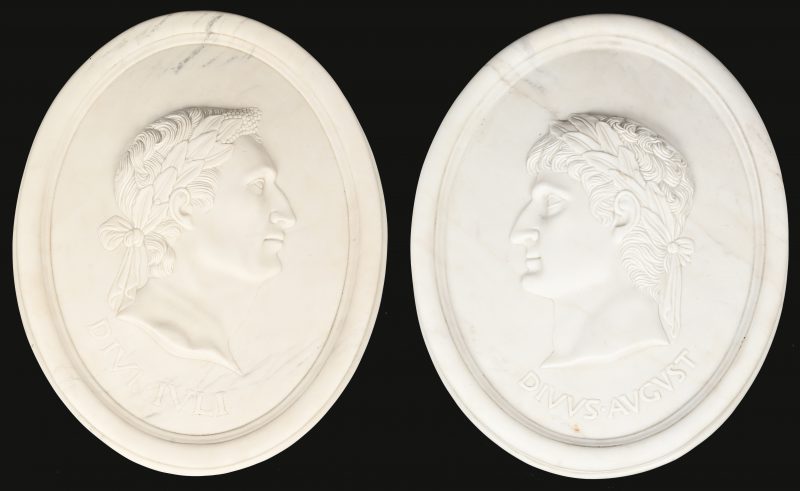 Een paar ovalen wandmedaillons in wit marmer, met in bas-reliëf de beeltenis van keizers Augustus en Julius.