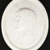 Een paar ovalen wandmedaillons in wit marmer, met in bas-reliëf de beeltenis van keizers Augustus en Julius.