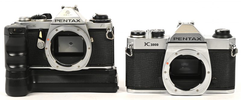 Een set van 2 vintage analoge Pentax camera’s zonder lens of beschermkap bestaande uit een K1000 en een ME met winder en documentatie.