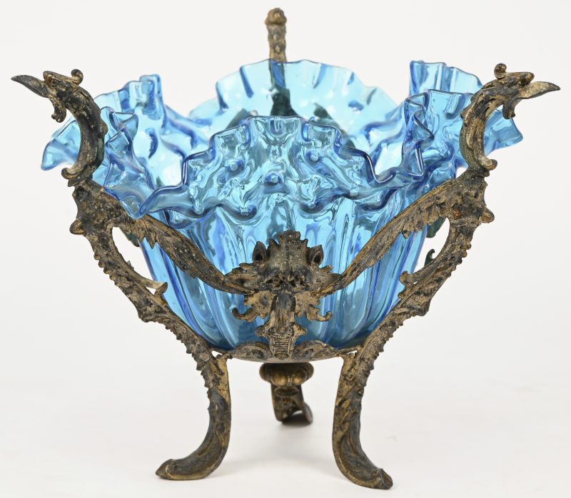 Blauwglazen organisch gevormde schaal, op driebenige vergulde metalen voet. Versierd met grifoenen en andere fabeldieren.