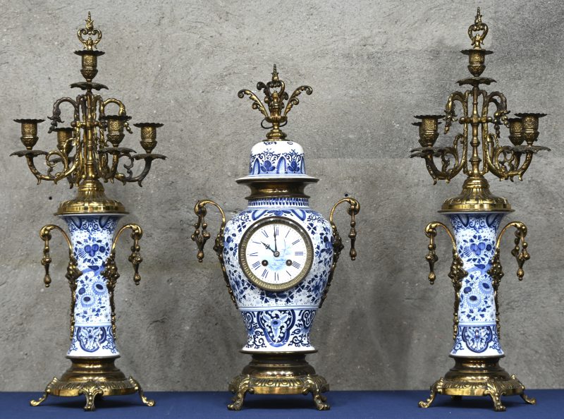 Een klokstel van blauw en wit Delfts aardewerk en koper, twee kandelaars met 5 lichtpunten.