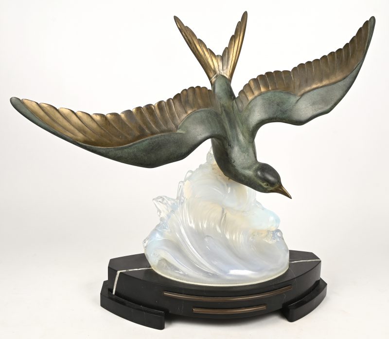 Een art-deco tafellamp bestaande uit een bronzen vogel op glazen golf en marmeren sokkel.