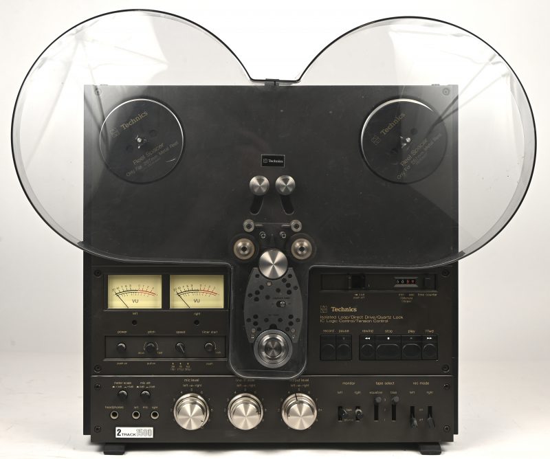 Een vintage bandrecorder, Technics RS 1500 US, geproduceerd tussen 1977 en 1983. Met de zeldzame plexiglazen beschermkap en beschermhoes, alsook de originele handleiding. Toegevoegd 2 lege zwart metalen reels van Technics. De adapters voor de grote reels manco.