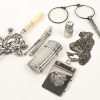 Een gevarieerd lot zilveren items met een variatie aan keuren bestaande uit een beker, een notaboekje, een halsketting, een luciferdoosje, een parfumflesje, een brievenklem, een haakje, een brilletje, een serveervork, een kadertje, een potlood en een rammelaar. 195 gram.