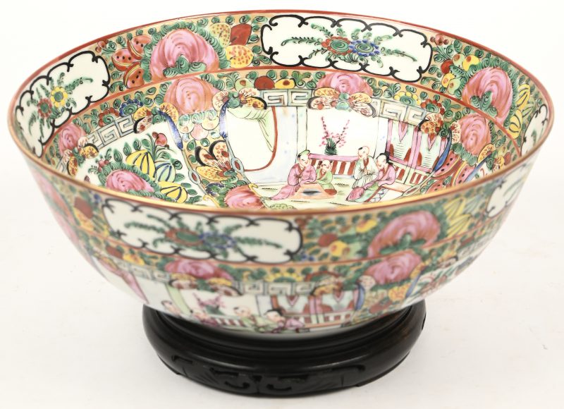 Een coupe van Chinees Canton porselein met een famille rose decor van pioenen en personages in interieurs in uitsparingen. Onderaan gemerkt en op houten sokkeltje.