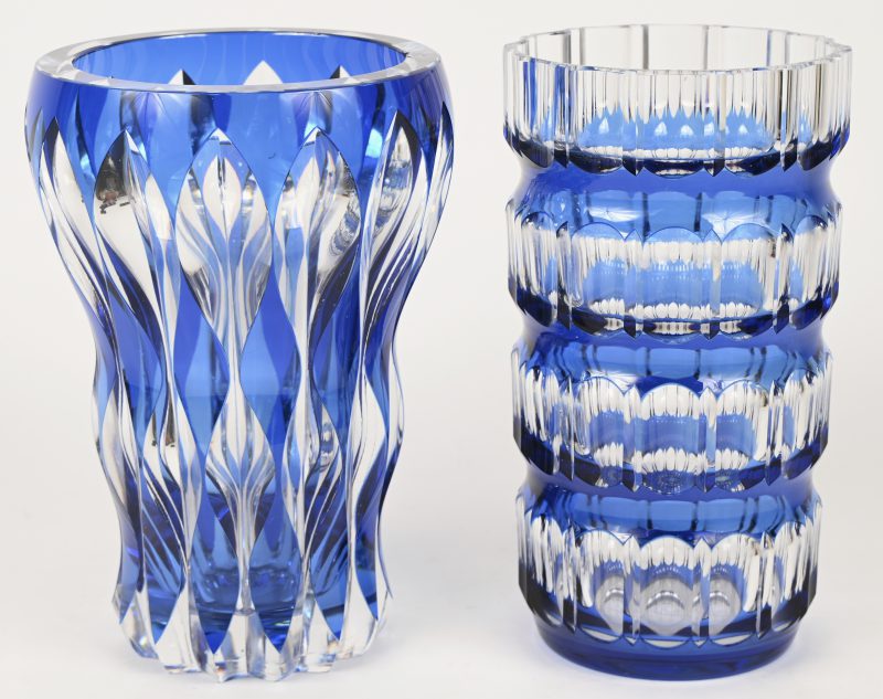 Twee vazen van geslepen kristal, blauw gekleurd in de massa. De ene cilindrisch ( H. 22.5 cm), de andere met een golfbeweging op de buik en een verbredende rand (23 cm, met schilfers boven en onderaan).