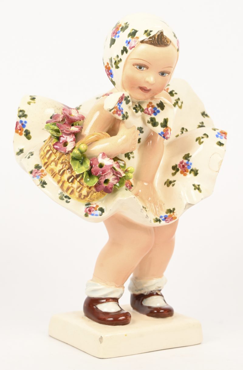 “Bloemenmeisje”. Een Italiaans beeldje van polychroom zachte pasta van een meisje met bloemenmand en opwaaiend jurkje, onderaan gemerkt. Beide benen bij de enkels gelijmd.