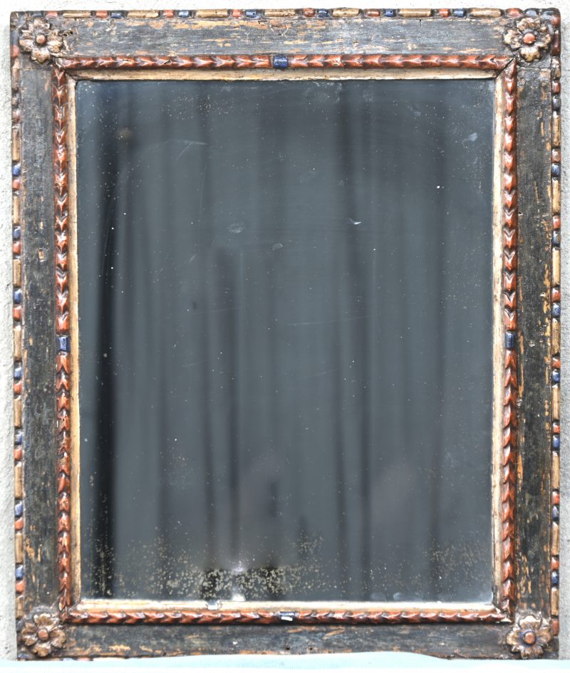 Een oude spiegel in polychrome gesculpteerde houten kader.
