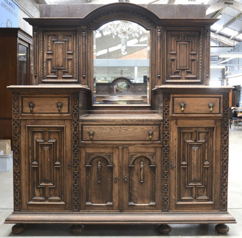 Een barok buffet van gebeeldhouwd eikenhout. Boven een geslepen spiegel  geflankeerd door twee panelen met penen op de stijlen. Onderaan twee grotere paneeldeuren, twee kleine deuren en drie laden.