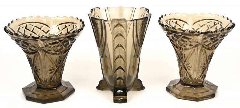 Drie greiskleurige vazen van gegoten glas, een paar op achthoekige voet (H. 17 cm) en één art deco model op drie pootjes (H. 20.5). Gemerkt “Belge”.