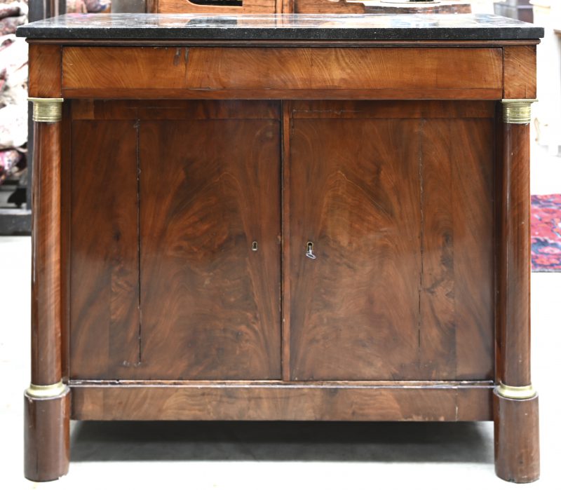 Antieke commode met zwart marmeren blad. Het front is geflankeerd door twee zuilen met messingen beslag. Twee deuren en één lade.