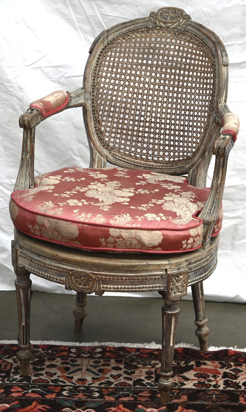 Antieke armstoel in Louis XV stijl. Gevlochten zitting en rug, met een roze kussen. Mooie ouderdomspatina.