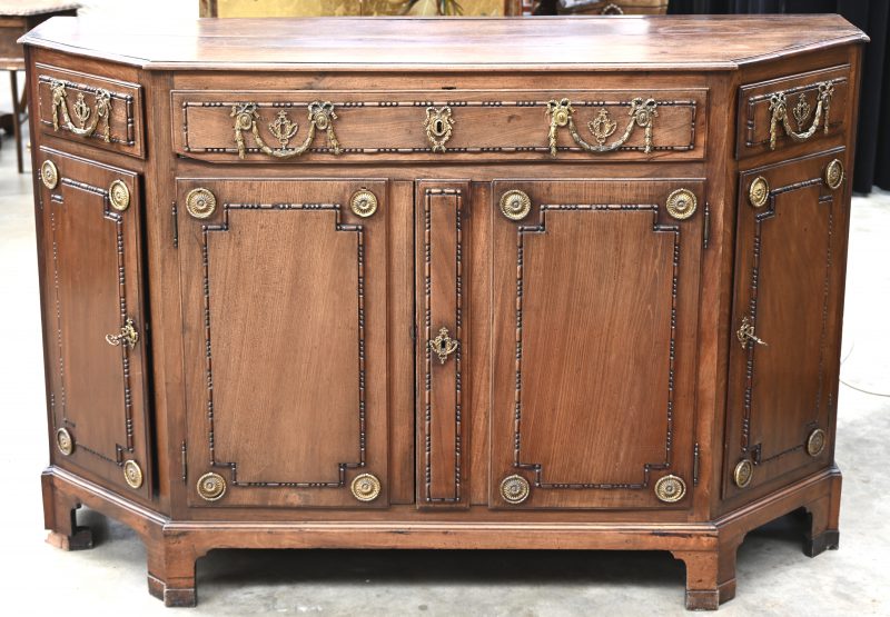 Commode in Empire stijl met afgeschuinde hoeken. Vier deuren, één grote lade vooraan en twee kleinene aan de schuine kant. Messing beslag.