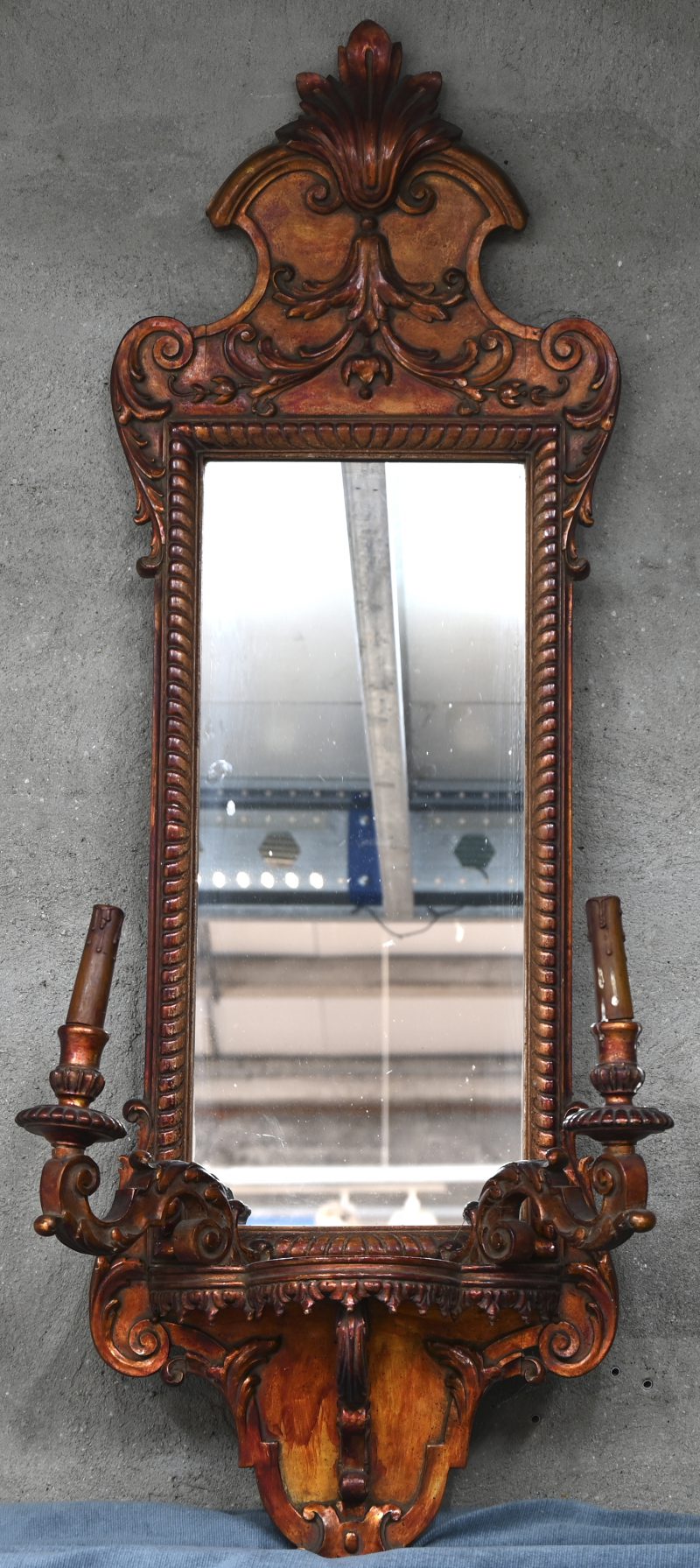 Een gebeitste houten spiegel in barokke stijl, met onderaan twee lichtpunten en een kleine console.