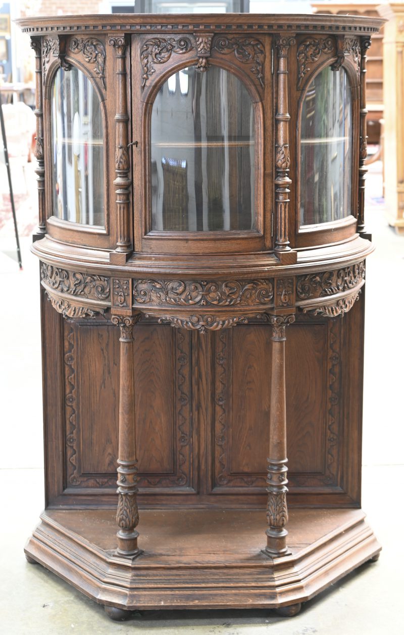 Een halfrond meubel met bovenaan vitrine met drie gebogen ruiten en één centrale deur. Onderaan open basis met vooraan twee Ionische zuilen. Mooie gebeeldhouwde friesen in barokke stijl.