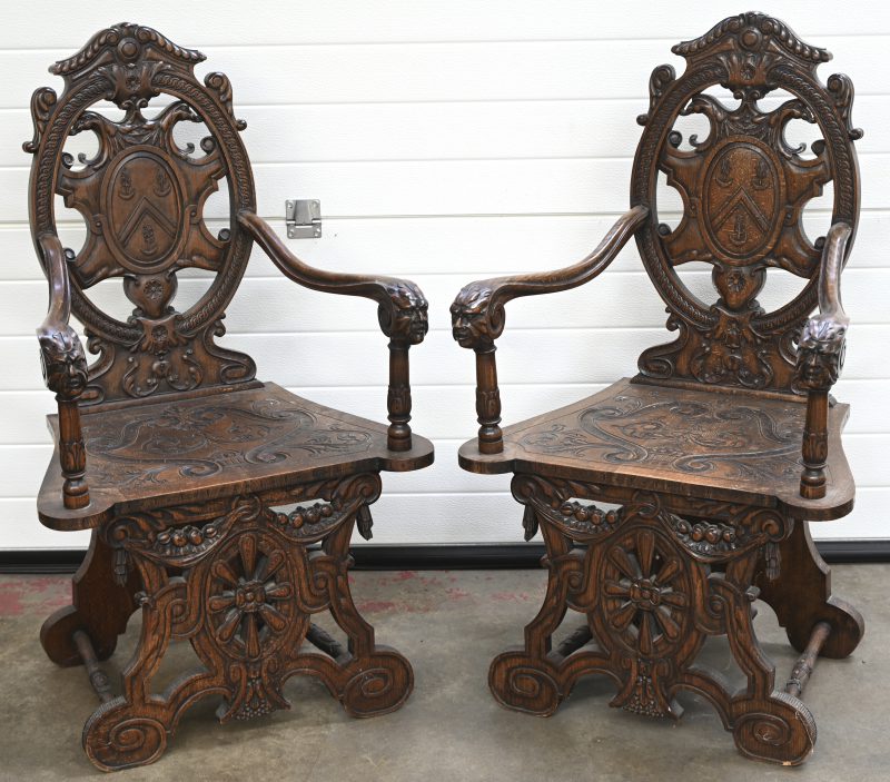 Een paar rijkelijke gebeeldhouwde eikenhouten stoelen. Gebogen armleuningen eindigend in hoofden, opengewerkte ruggen en voorste poten met een wielmotief en een wapenschild.