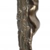 Een bronzen beeldje van een naakte dame gekneveld aan een boomstronk.